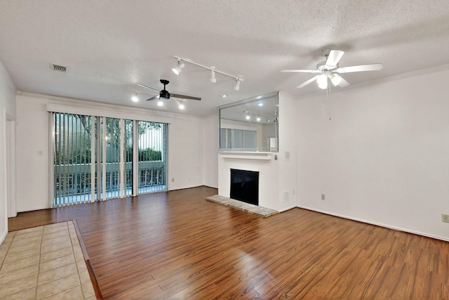 unfurnished living room featuring a ceiling fan, wood finished floors, a textured ceiling, a glass covered fireplace, and crown molding