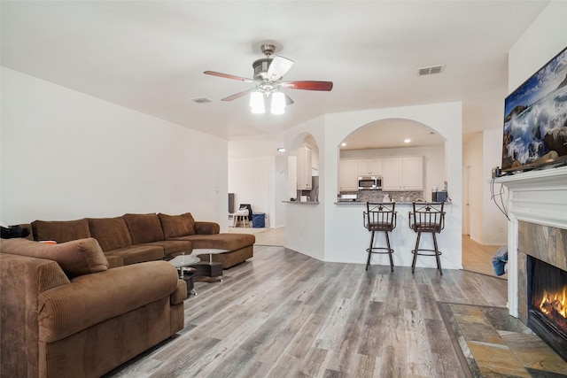 8652 Fernhill Dr, Fort Worth, TX 76123 - living room with arched walkways, wood finished floors, a premium fireplace, and a ceiling fan