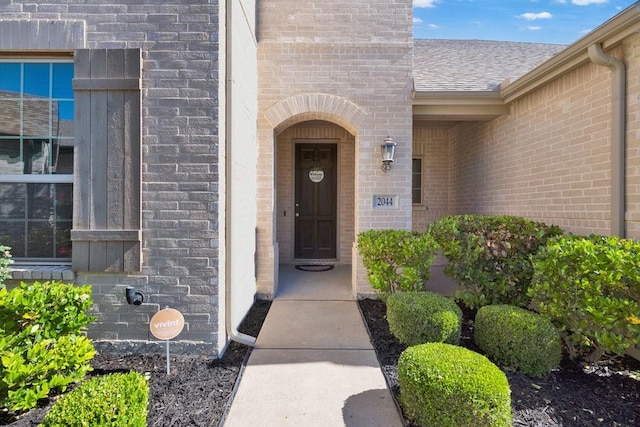 property entrance featuring brick siding and roof with shingles