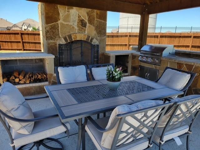 view of patio / terrace featuring an outdoor stone fireplace, fence, a grill, and area for grilling