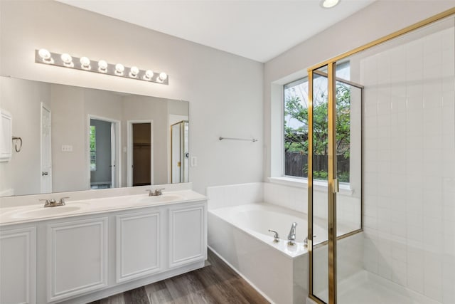 full bath with a bath, a stall shower, double vanity, and wood finished floors