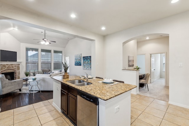 kitchen featuring dishwasher, light tile patterned floors, open floor plan, arched walkways, and a stone fireplace