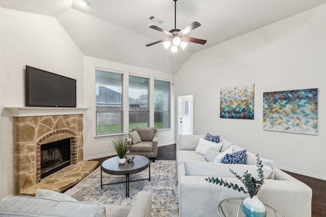 living room with vaulted ceiling, wood finished floors, baseboards, ceiling fan, and a stone fireplace