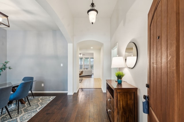 foyer with arched walkways, dark wood finished floors, and baseboards