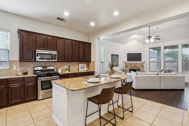 kitchen featuring appliances with stainless steel finishes, a sink, light stone countertops, open floor plan, and a ceiling fan