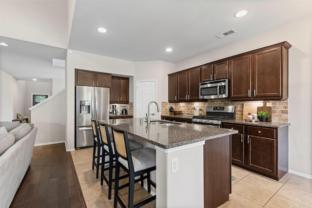1744 Wildflower Ln, Wylie, TX 75098 - kitchen with stainless steel appliances, a sink, a kitchen bar, tasteful backsplash, and dark brown cabinetry