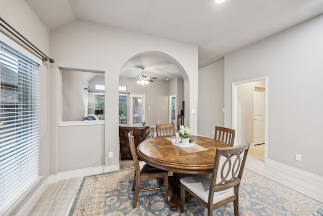 dining space with light wood-style flooring, a ceiling fan, arched walkways, baseboards, and lofted ceiling