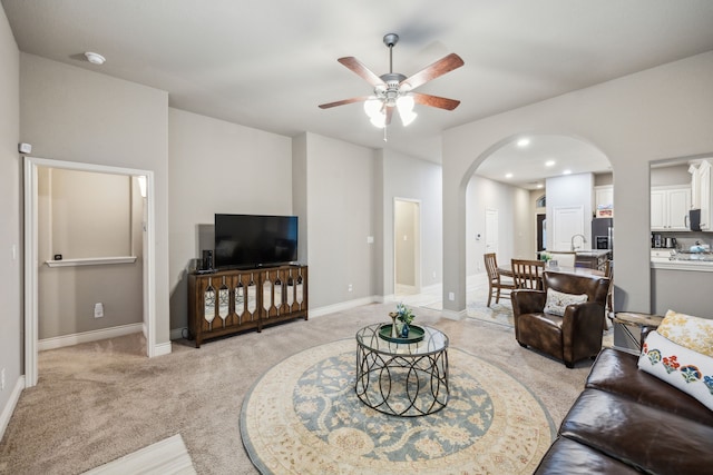 living room with light colored carpet, ceiling fan, arched walkways, and baseboards