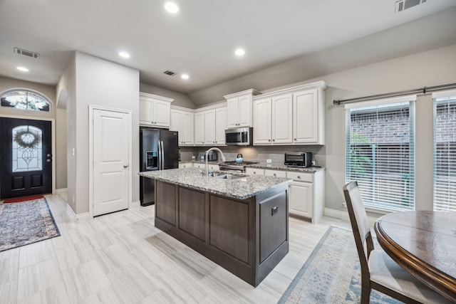kitchen featuring stainless steel appliances, a sink, white cabinetry, light stone counters, and a kitchen island with sink