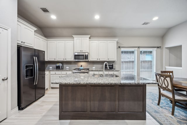 kitchen featuring stainless steel appliances, a sink, white cabinets, light stone countertops, and an island with sink