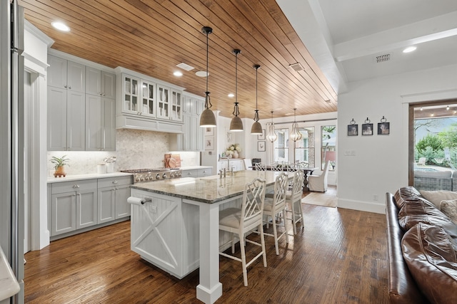 304 Nora Ln, Argyle, TX 76226 - kitchen with wood ceiling, a center island, a kitchen bar, backsplash, and light stone counters