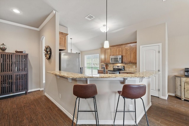 2134 Sagewood Dr, Weatherford, TX 76087 - kitchen with appliances with stainless steel finishes, a kitchen breakfast bar, dark wood-style flooring, light stone counters, and ornamental molding