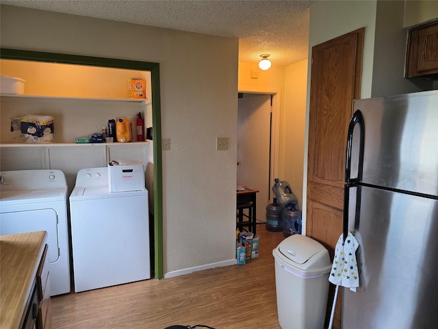 laundry area with separate washer and dryer, light wood-type flooring, baseboards, and a textured ceiling