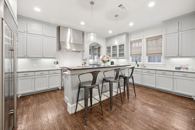 3728 Stanford Ave, University Park, TX 75225 - kitchen featuring wall chimney exhaust hood, a kitchen bar, dark wood-type flooring, premium appliances, and decorative backsplash