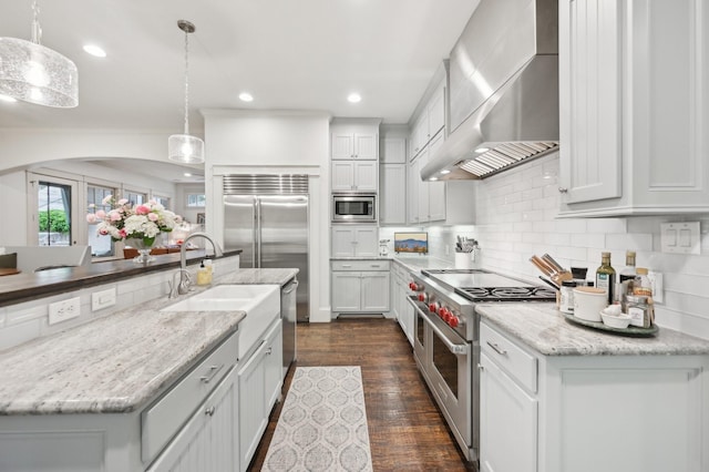 3728 Stanford Ave, University Park, TX 75225 - kitchen featuring appliances with stainless steel finishes, wall chimney exhaust hood, a sink, decorative backsplash, and hanging light fixtures