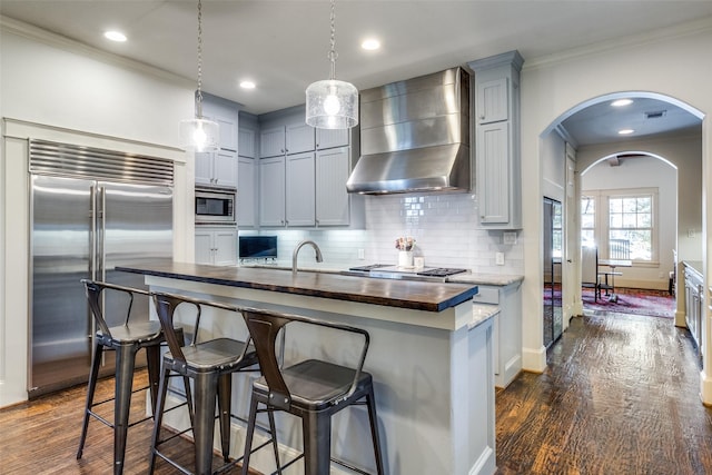 3728 Stanford Ave, University Park, TX 75225 - kitchen featuring built in appliances, wall chimney range hood, ornamental molding, arched walkways, and dark wood-style floors