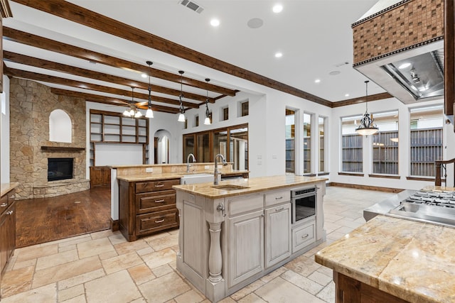 kitchen with a kitchen island with sink, open floor plan, a fireplace, light countertops, and stone tile flooring