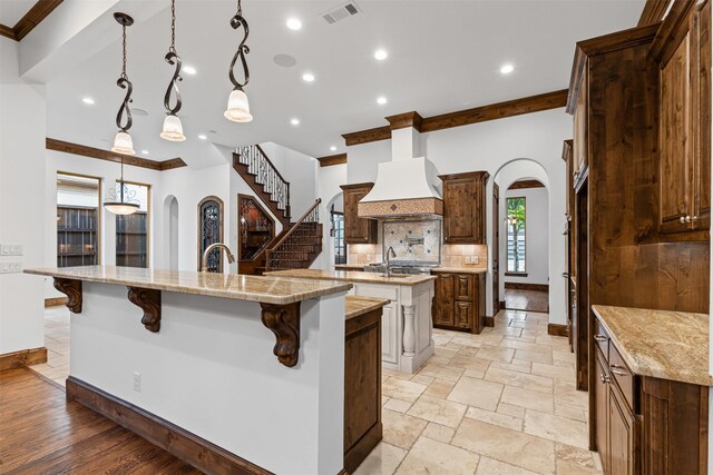 kitchen featuring a large island, arched walkways, premium range hood, crown molding, and backsplash
