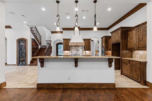 kitchen with arched walkways, stainless steel oven, decorative backsplash, a breakfast bar area, and custom exhaust hood