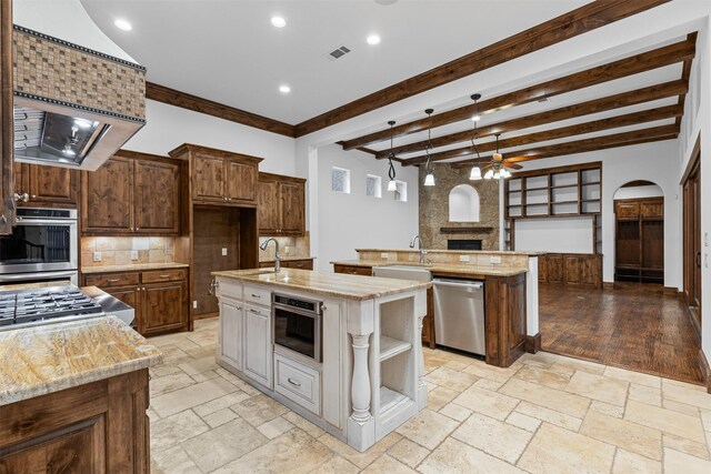 kitchen with appliances with stainless steel finishes, a center island with sink, a sink, decorative backsplash, and a ceiling fan