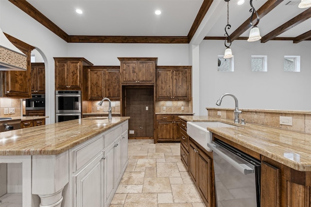 kitchen featuring appliances with stainless steel finishes, a spacious island, ornamental molding, a sink, and stone tile flooring