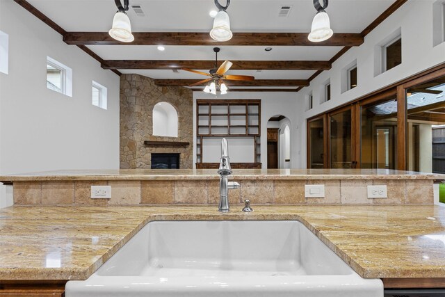 kitchen with a sink, beamed ceiling, a fireplace, arched walkways, and a ceiling fan