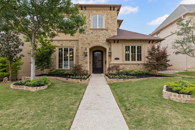 view of front of property with stone siding, a front lawn, stucco siding, and roof with shingles