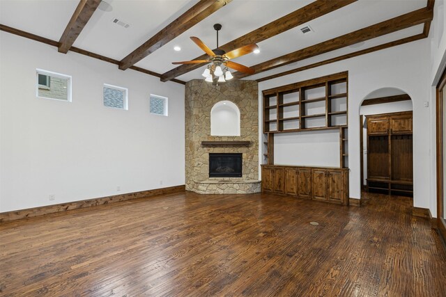 unfurnished living room with a ceiling fan, wood-type flooring, arched walkways, beam ceiling, and a stone fireplace