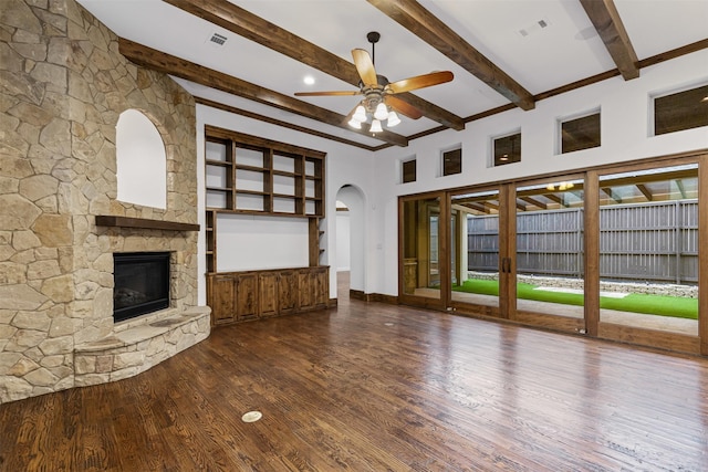 unfurnished living room with a fireplace, a ceiling fan, wood finished floors, beam ceiling, and arched walkways