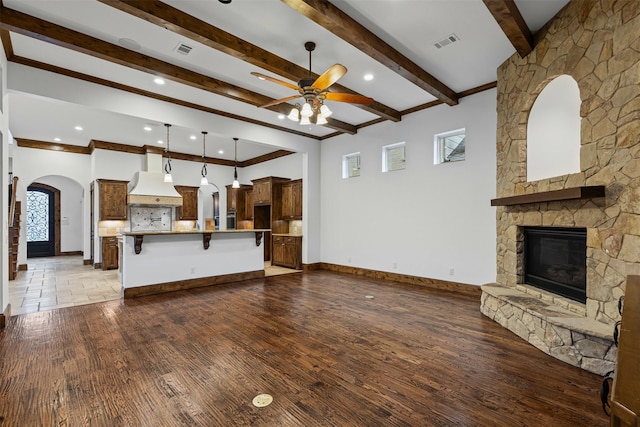 unfurnished living room featuring a ceiling fan, arched walkways, plenty of natural light, a fireplace, and beamed ceiling
