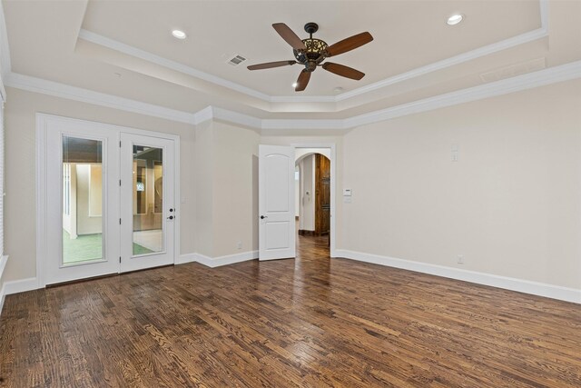spare room featuring a tray ceiling, wood finished floors, arched walkways, a ceiling fan, and crown molding
