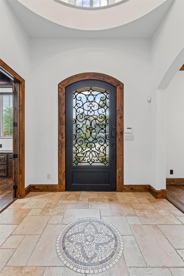 foyer with stone tile floors, baseboards, a towering ceiling, and arched walkways