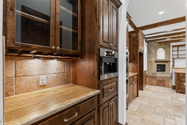 kitchen featuring dark brown cabinetry, beam ceiling, stone tile floors, a fireplace, and light countertops