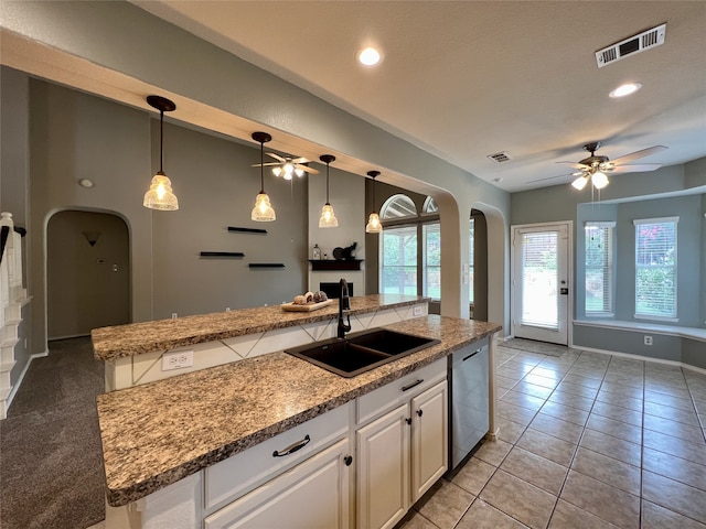 kitchen featuring arched walkways, stainless steel dishwasher, a sink, ceiling fan, and white cabinetry