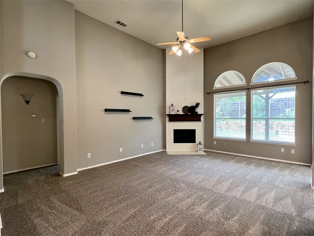unfurnished living room with a towering ceiling, dark carpet, a ceiling fan, baseboards, and arched walkways