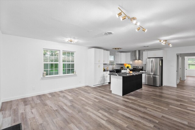 kitchen featuring stainless steel appliances, wall chimney range hood, a kitchen island, white cabinetry, and tasteful backsplash