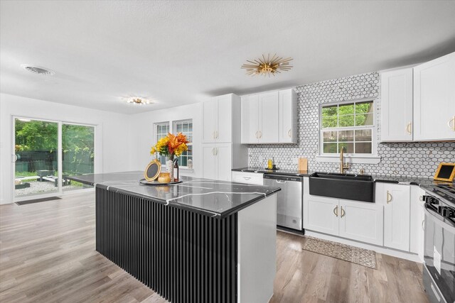 kitchen with dishwasher, a sink, dark countertops, gas range, and white cabinetry