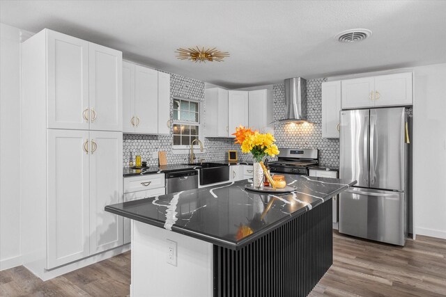 kitchen with appliances with stainless steel finishes, wall chimney exhaust hood, a sink, dark countertops, and white cabinets