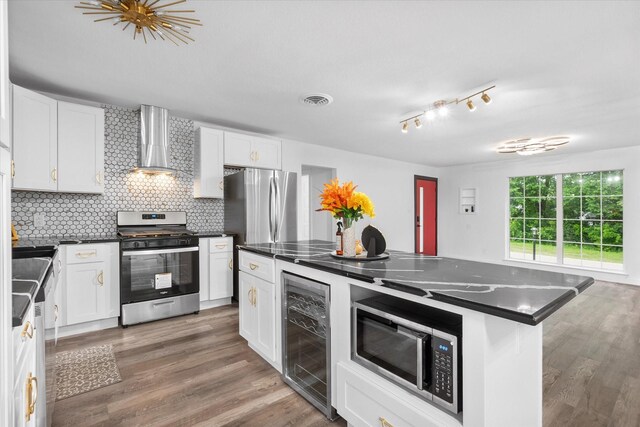 kitchen with appliances with stainless steel finishes, wall chimney range hood, beverage cooler, dark countertops, and backsplash