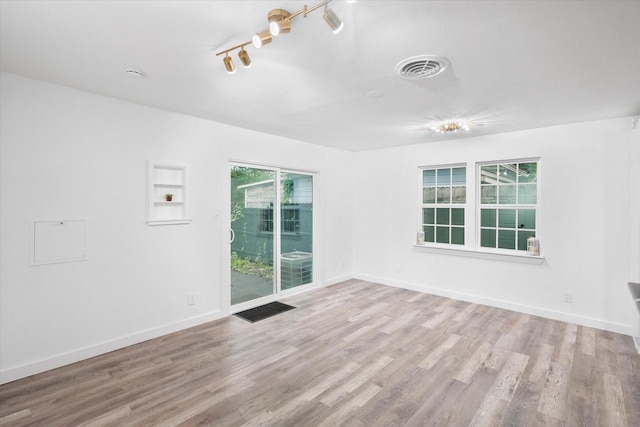 empty room featuring wood finished floors, baseboards, and rail lighting