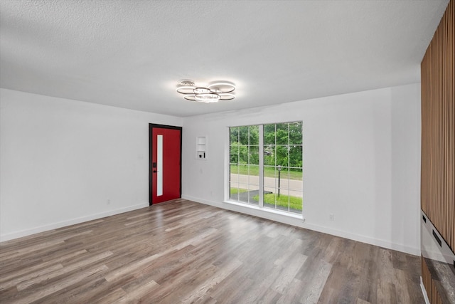 unfurnished living room featuring wood finished floors, a chandelier, baseboards, and a textured ceiling