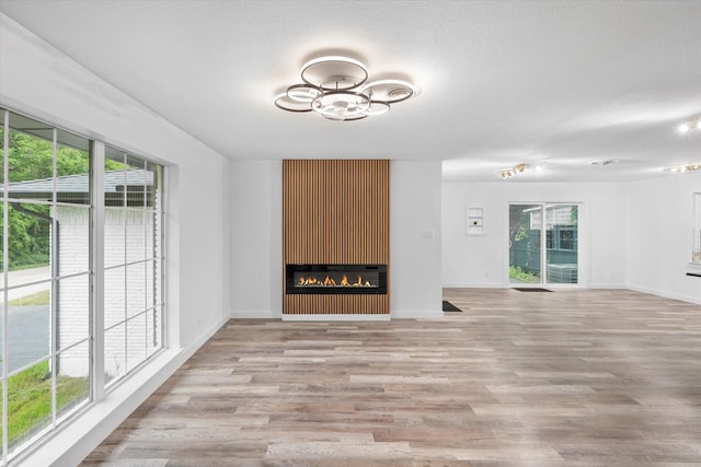 unfurnished living room featuring light wood-style flooring, baseboards, and a glass covered fireplace