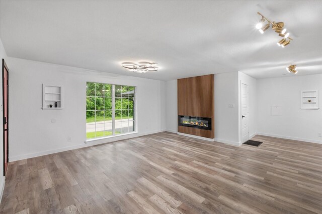 unfurnished living room featuring a large fireplace, light wood-type flooring, and baseboards