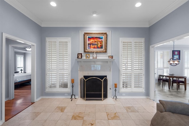 living room featuring crown molding, healthy amount of natural light, a premium fireplace, a chandelier, and baseboards