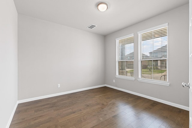 empty room featuring healthy amount of natural light, baseboards, and dark wood-style flooring