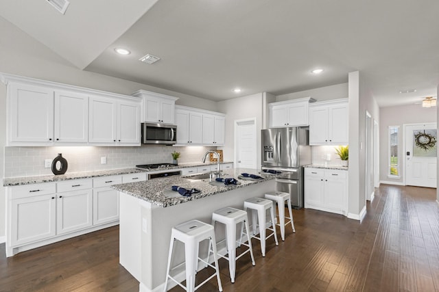 kitchen with appliances with stainless steel finishes, a sink, tasteful backsplash, a breakfast bar area, and white cabinets