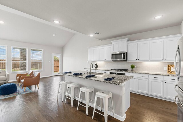 kitchen featuring stainless steel appliances, vaulted ceiling, a sink, tasteful backsplash, and a kitchen breakfast bar