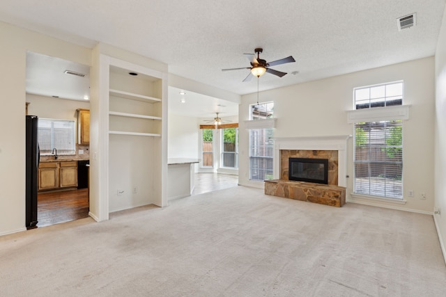 10008 Preston Vineyard Dr, Frisco, TX 75035 - unfurnished living room with ceiling fan, light carpet, a tiled fireplace, baseboards, and a sink