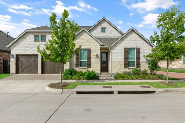 view of front of house with driveway, stone siding, a shingled roof, an attached garage, and brick siding