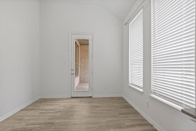 spare room featuring light wood finished floors, lofted ceiling, healthy amount of natural light, and baseboards